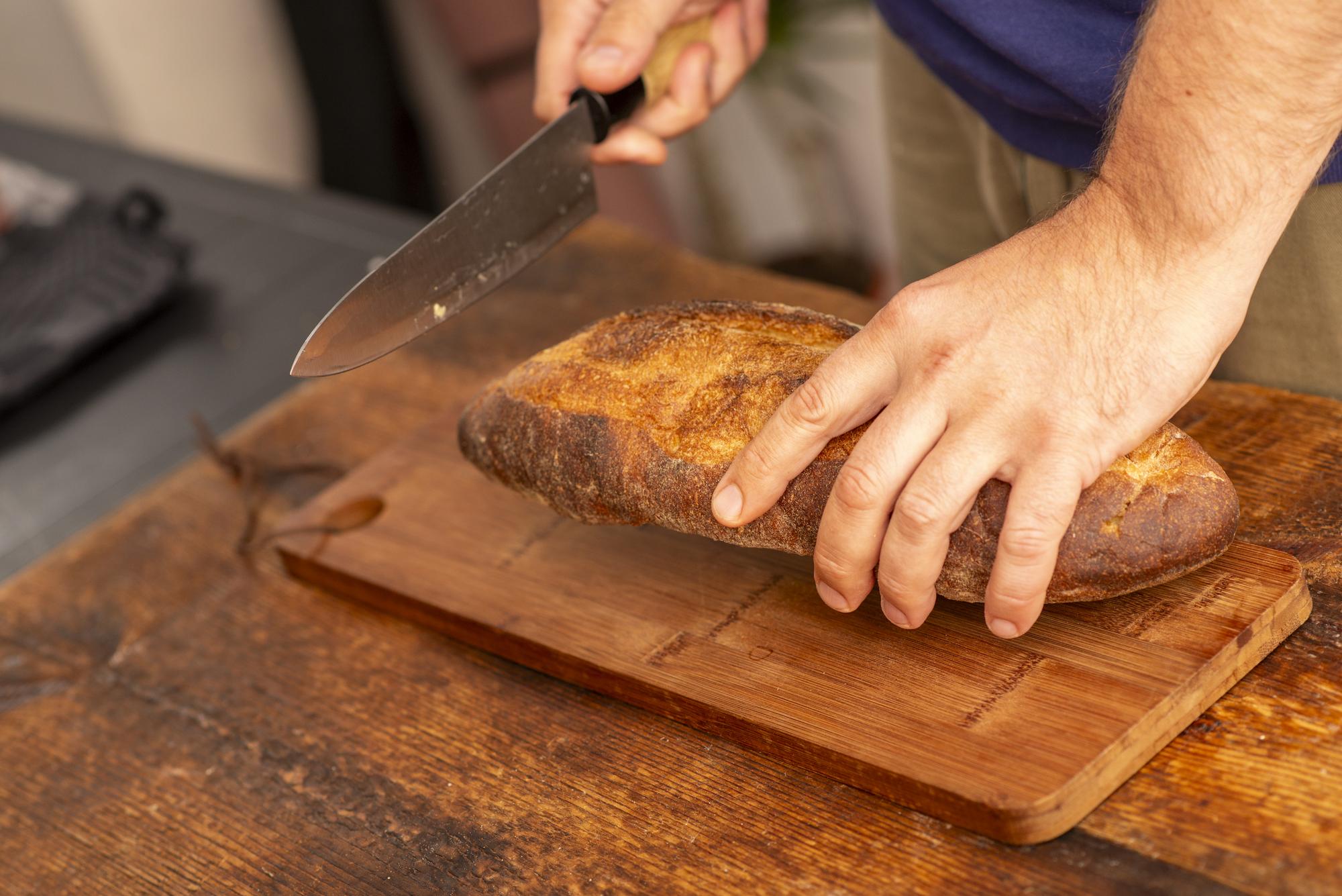 Hands slicing fresh loaf on wooden board